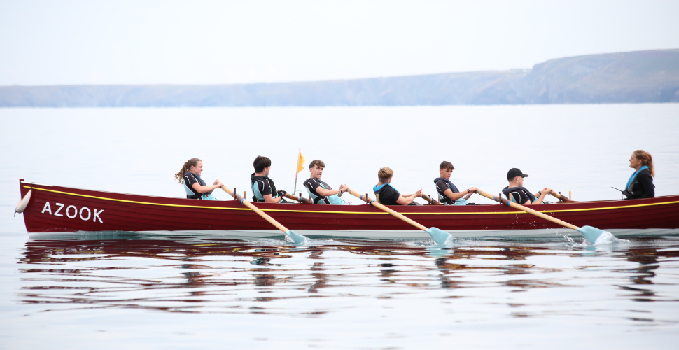 Men rowing on a gig boat with water on the bottom half of the image